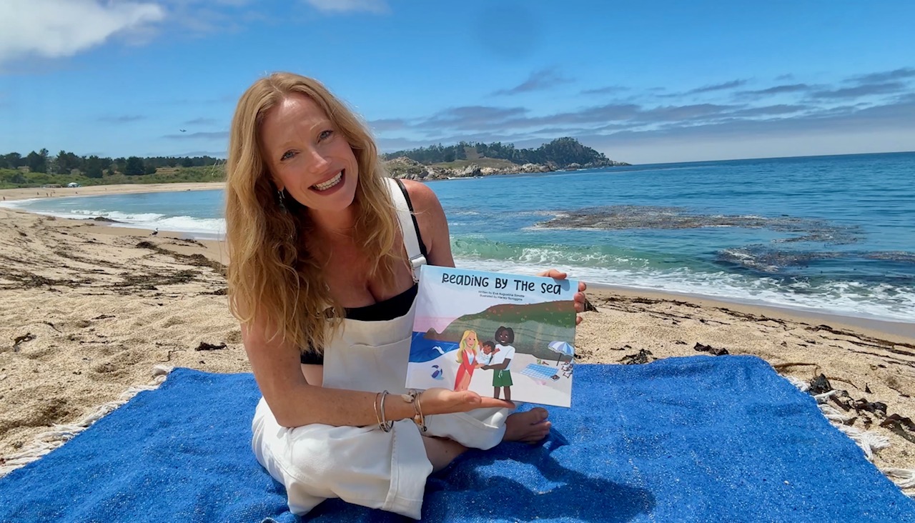 Eva Augustina Sinotte on a blue blanket at the beach holding Reading By The Sea